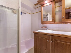 Une salle de bain dotée d’une douche à parois de verre, d’une baignoire blanche, d’un meuble-lavabo en bois et d’un miroir au-dessus du meuble-lavabo.