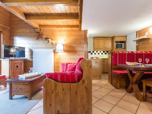 L’intérieur chaleureux d’un chalet avec une table à manger en bois, des sièges rembourrés de couleur rouge, un téléviseur et un coin cuisine.