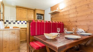 Een houten keuken met een eettafel gedekt voor twee personen, een rode gewatteerde bank en een magnetron boven het aanrecht.
