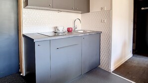 Uma cozinha compacta com armários cinzas, uma pia de aço inoxidável e bancada.