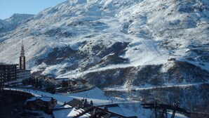 Montanha coberta de neve com uma estação de esqui em primeiro plano, com edifícios e teleféricos.