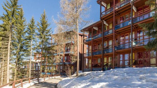 Un edificio de madera de varios pisos con balcones, rodeado de nieve y árboles.