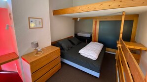 Un dormitorio pequeño con una cama litera, una mesita de noche con lámpara y un aparador.