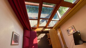 Una habitación compacta con tragaluz, un sofá rojo con lunares, un banco de madera y un cuadro en la pared.