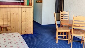 A small, cozy room with a wooden bed, a dining table with chairs, a microwave, and a small kitchenette.