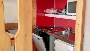 A compact kitchen with a red backsplash, stainless steel appliances, and wooden accents.