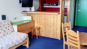 A compact room with a bed, a desk with a computer, a chair, and a small stool.