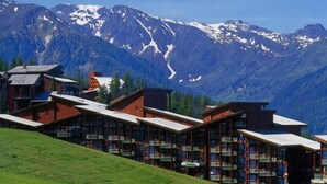 A hotel with multiple buildings, each with a sloped roof and large windows, set against a backdrop of snow-capped mountains.
