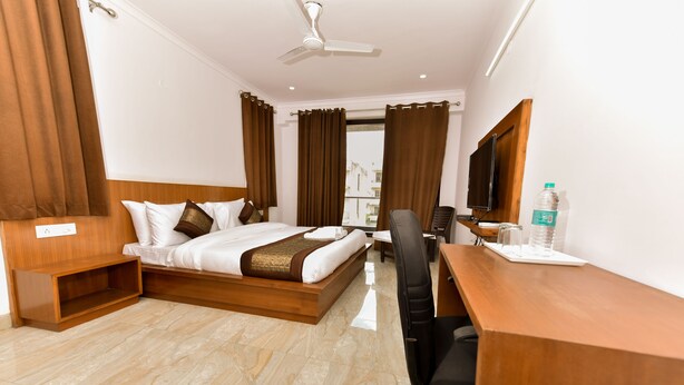 A hotel room with a bed, a desk, a chair, a television, and a water bottle. - Hotel Noida International (Noida)
