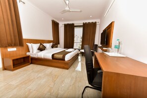 A hotel room with a bed, a desk, a chair, a television, and a water bottle. - Hotel Noida International (Noida)