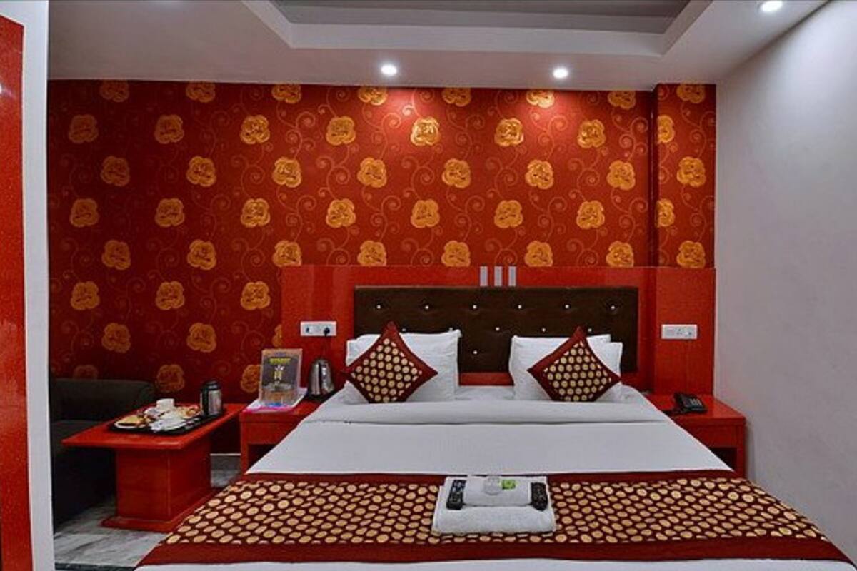 Habitación de hotel con una cama grande, dos mesitas de noche, un muro con estampado rojo y dorado, y una lámpara en el techo.