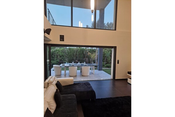 Uma sala de estar moderna com uma grande janela de vidro que dá para uma área de refeições ao ar livre.