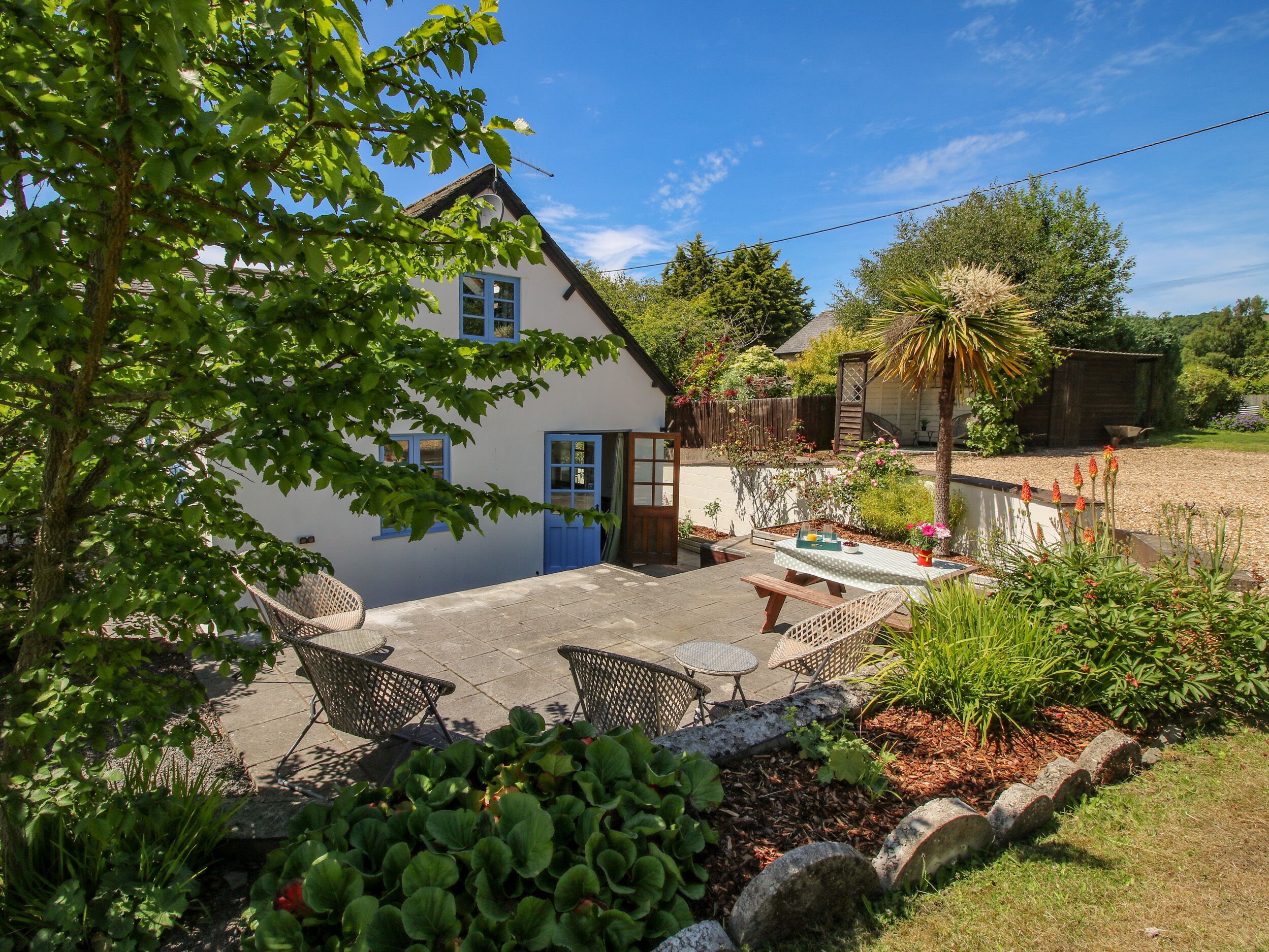 A house with a blue door, a patio with chairs, and a garden with plants and a palm tree.