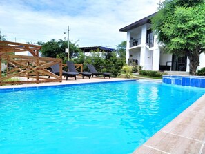 A swimming pool with lounge chairs, a wooden pergola, and a two-story building with balconies. - The Boathouse at Calatagan (Calatagan)