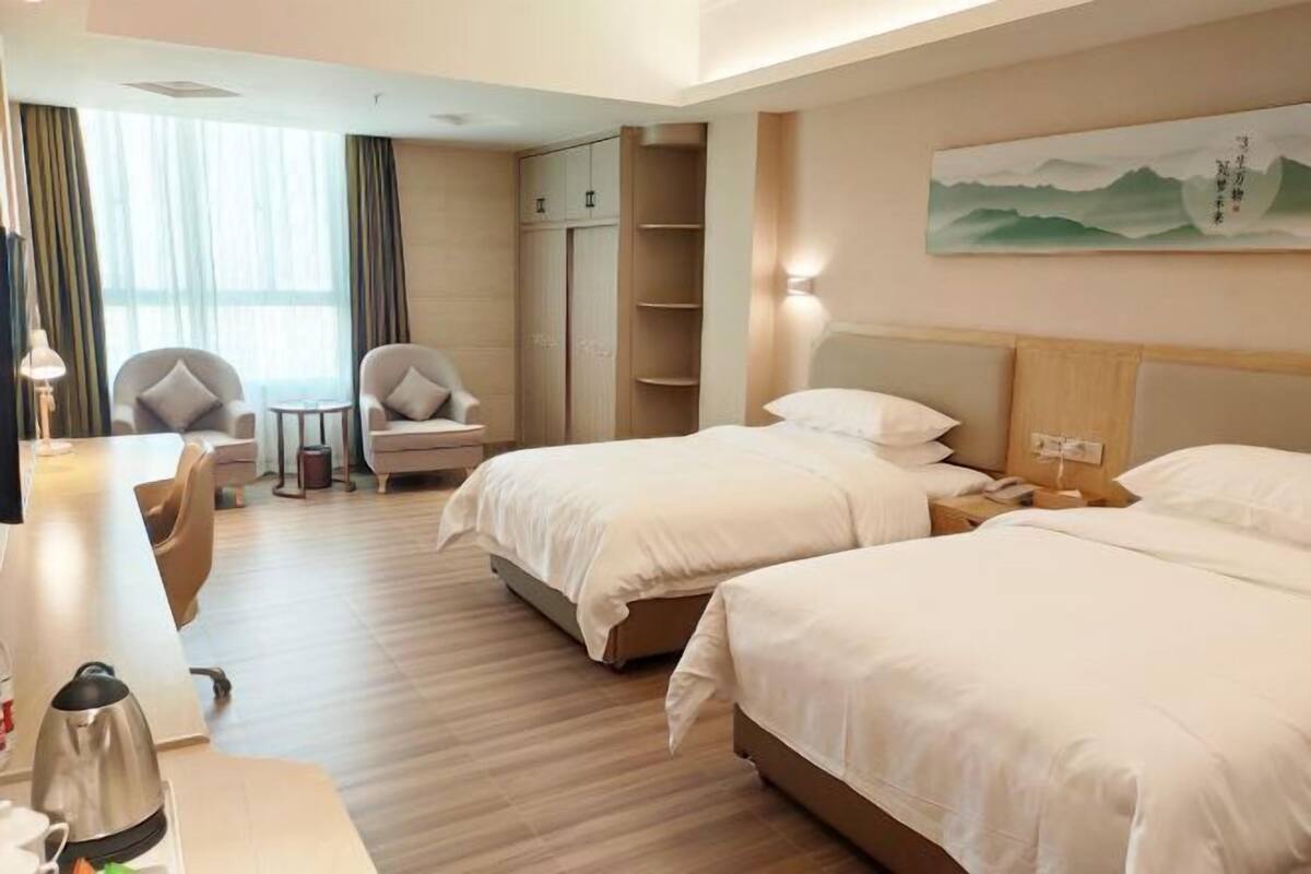 Ein Hotelzimmer mit zwei Betten, einem Schreibtisch, einem Stuhl, einem Kleiderschrank und einem Bild an der Wand.