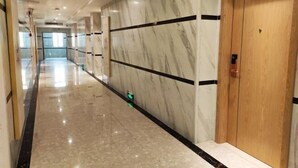 A corridor with marble walls, a wooden door, and a reflective floor. - Xin Zhenhao Business Hotel (Shantou)