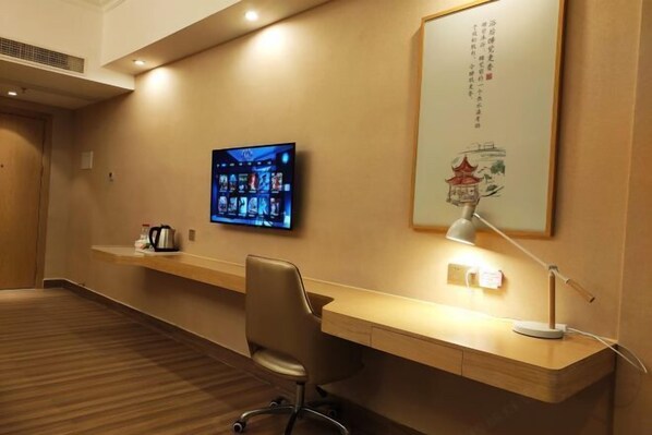 Habitación de hotel con un escritorio de madera, una silla, un televisor de pantalla plana en la pared, una lámpara y un adorno mural.