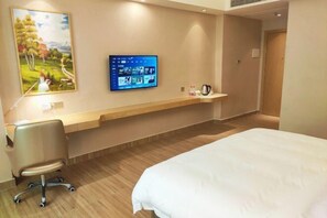 A hotel room with a bed, a desk, a chair, a mounted TV, and a shelf with toiletries. - Xin Zhenhao Business Hotel (Shantou)