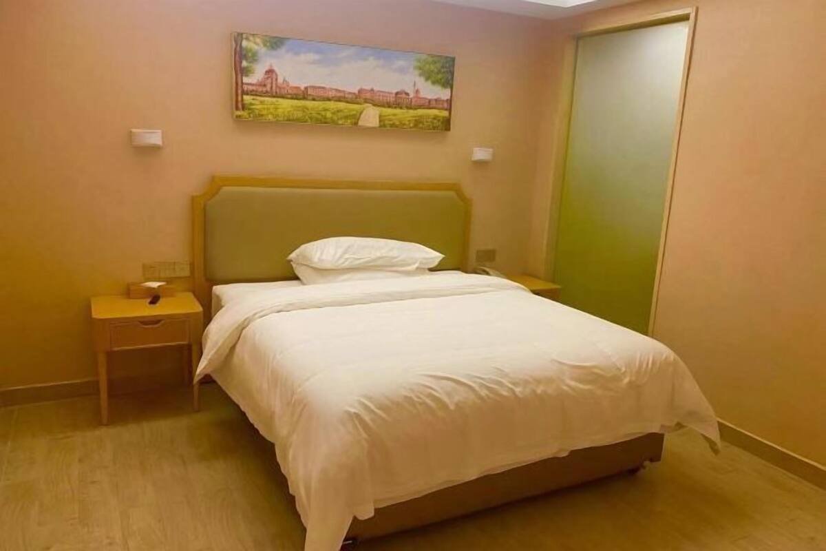 Ein Hotelzimmer mit einem Einzelbett, einem Nachttisch, einem Bild an der Wand und einer grünen Tür.