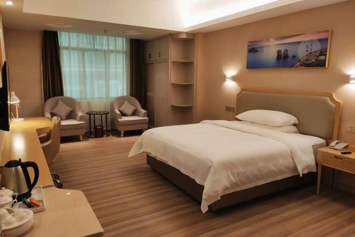Ein Hotelzimmer mit einem großen Bett, zwei Sesseln, einem Schreibtisch mit Lampe, einer Kaffeemaschine und einem Bild an der Wand.