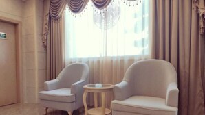 A room with two armchairs and a small round table, a chandelier, and a large window with curtains. - Xin Zhenhao Business Hotel (Shantou)