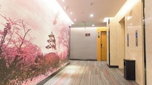 Un couloir orné d’une fresque représentant des fleurs de cerisier et une pagode, doté d’un revêtement de sol en moquette et d’un ascenseur situé sur le côté droit.