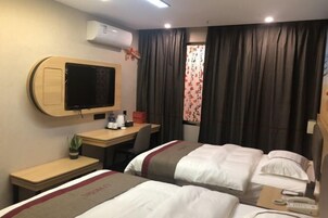 A hotel room with two beds, a desk with a chair, a television, and an air conditioning unit.