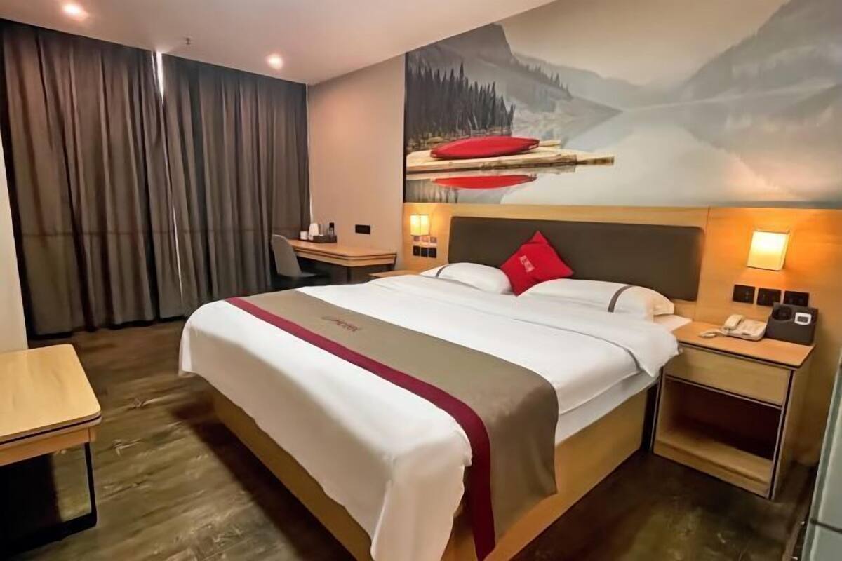 Une chambre d’hôtel avec un grand lit, un bureau, une chaise, une table de chevet et une fresque murale.