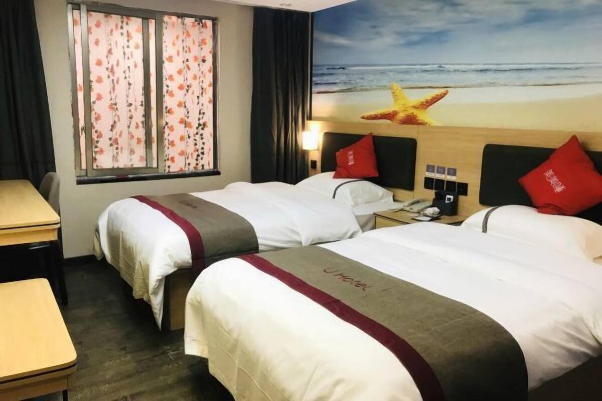 Une chambre d’hôtel avec deux lits, un bureau et une fenêtre agrémentée de rideaux à motifs floraux.