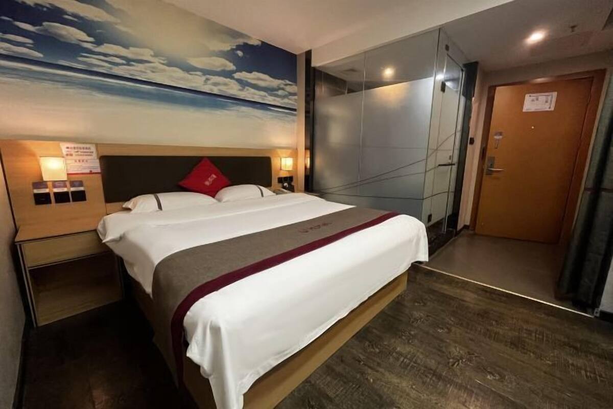 Une chambre d’hôtel avec un lit, une table de chevet, un téléviseur fixé au mur et une porte.