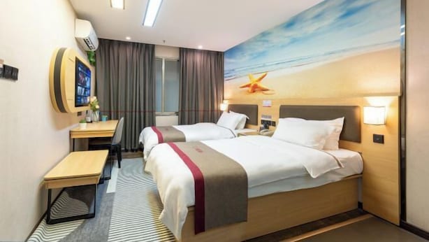 Une chambre d’hôtel avec deux lits, un bureau, une chaise, une télévision et une fresque murale sur le thème de la plage.