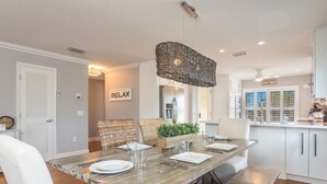A dining area with a rustic wooden table, white upholstered chairs, and a woven pendant light. - Seahorse Dreams by Beach Boutique Rentals (Bradenton Beach)