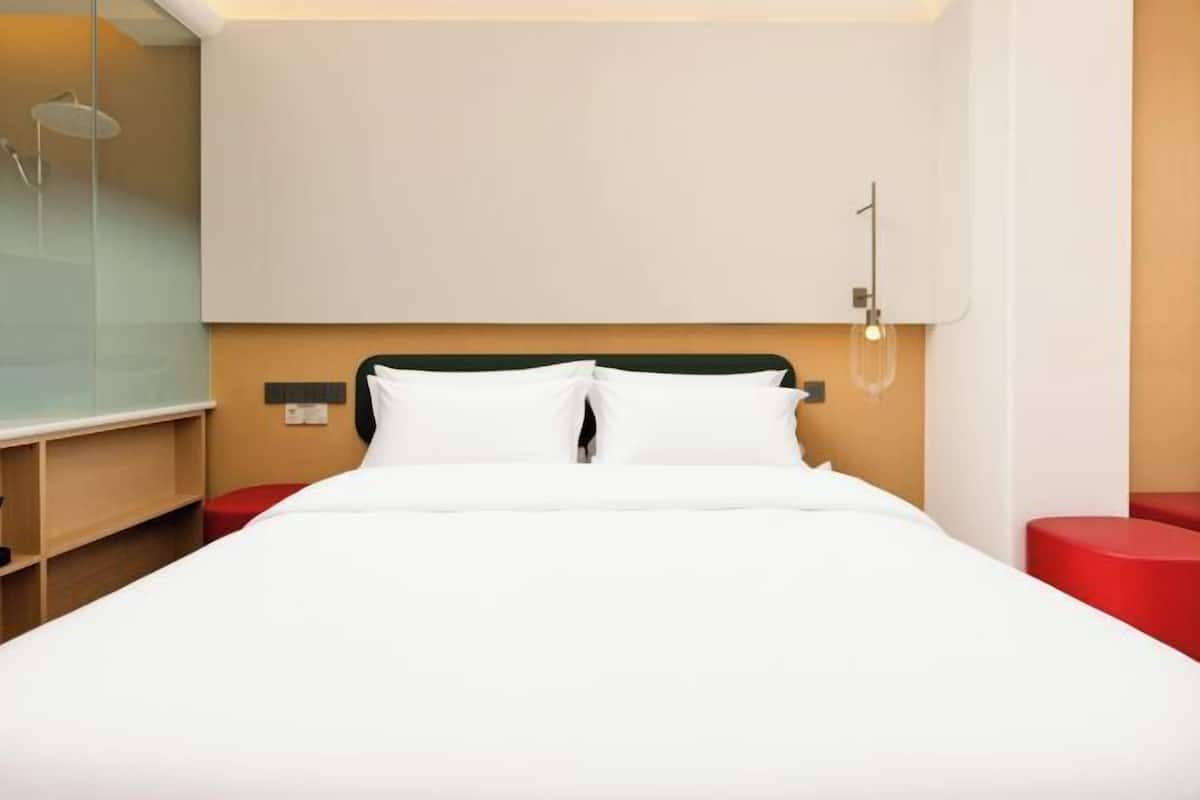 Ein modernes Hotelzimmer mit einem großen Bett, einer Duschkabine aus Glas und einer roten Akzentwand.