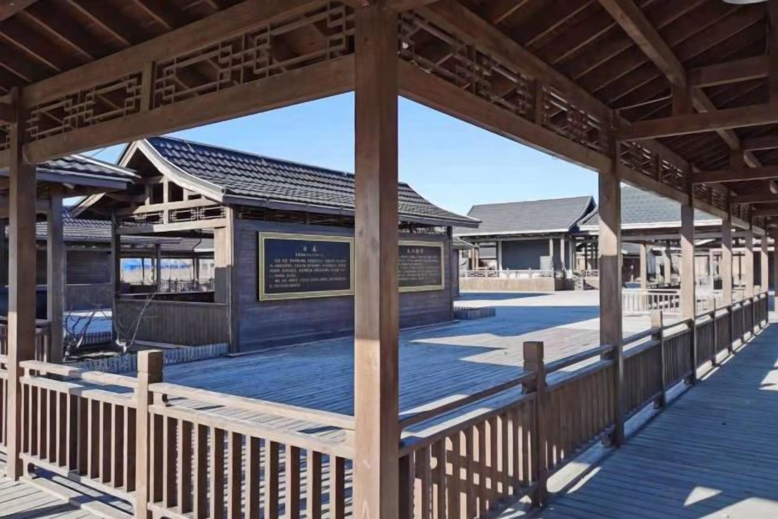 A wooden deck with a covered area, a building with a sign, and a clear sky.
