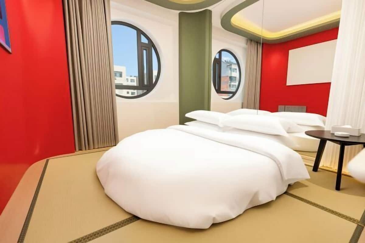 Ein modernes Hotelzimmer mit einem großen Bett, einem kleinen Tisch und zwei Fenstern.