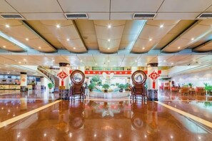 A spacious lobby with a polished floor, a central fountain, and a staircase leading to upper levels.