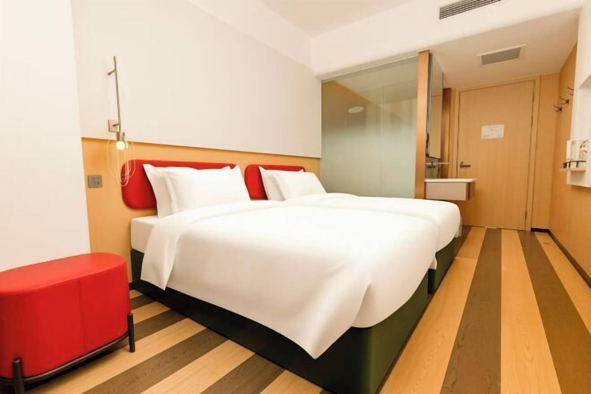 Ein Hotelzimmer mit einem Bett, einer roten Bank, einem Spiegel und einem kleinen Waschbecken.