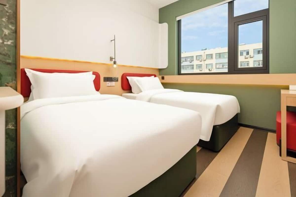 Ein Hotelzimmer mit zwei Betten, einem Fenster mit Blick auf Gebäude und einem roten Sessel.