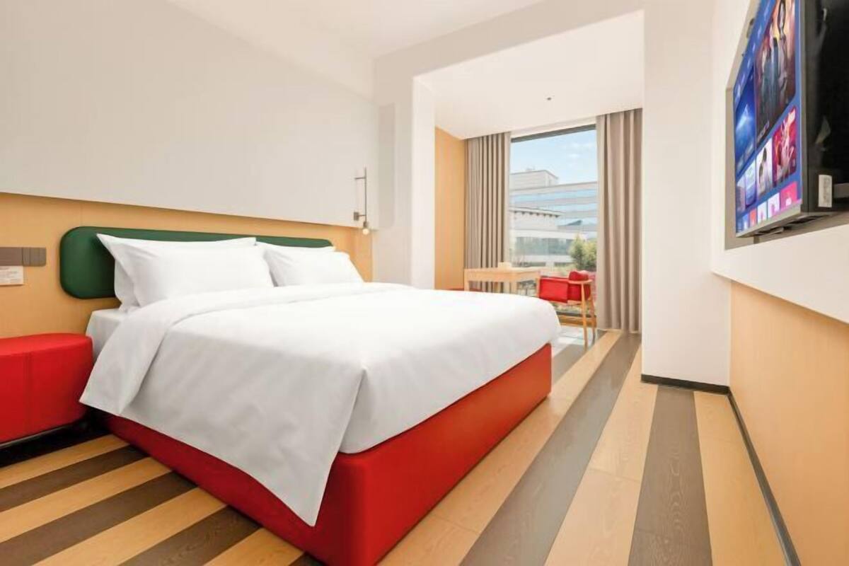 Ein Hotelzimmer mit Bett, einem roten Sessel, einem Fernseher und Blick auf die Stadt.