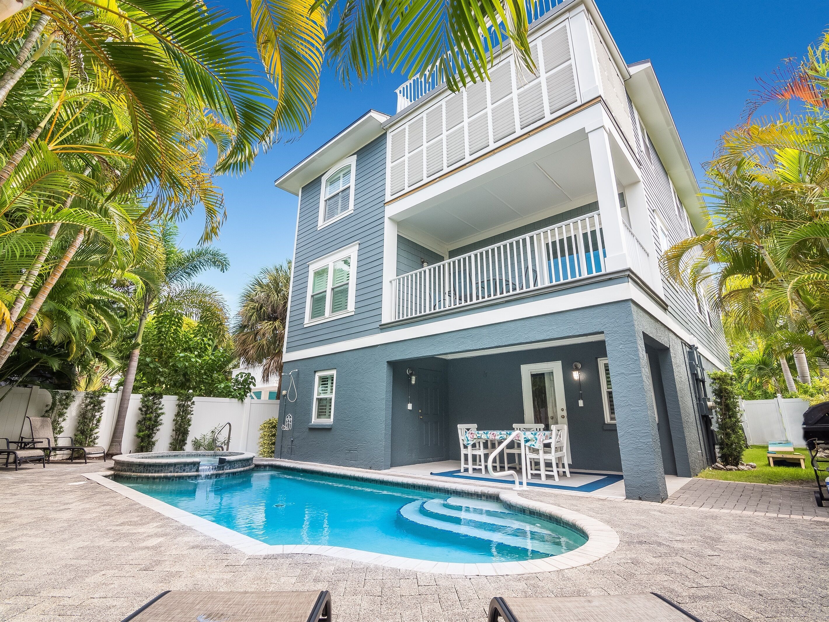 A two-story house with a swimming pool, a balcony, and a patio area with outdoor furniture.