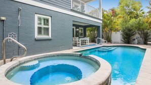 Une piscine avec un jacuzzi, entourée d’une maison dotée d’un balcon et de mobilier d’extérieur.