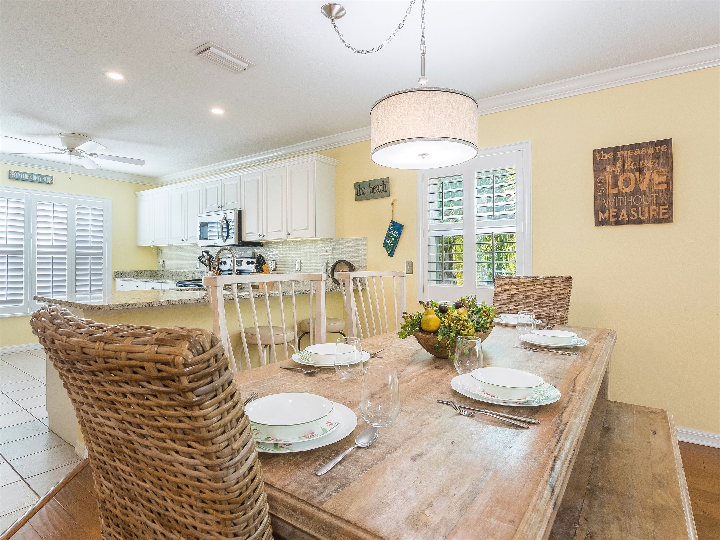A dining area with a wooden table set for four, surrounded by wicker chairs.