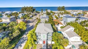 Une vue aérienne d’un quartier résidentiel situé sur la côte, avec des maisons, une grande maison blanche dotée d’une porte rouge, et une vue dégagée sur l’océan.