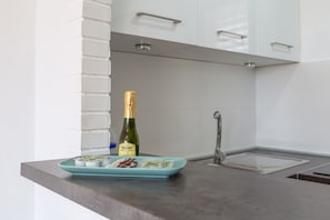 Une cuisine avec des meubles blancs, un plan de travail gris, une bouteille de champagne et une assiette contenant des aliments.