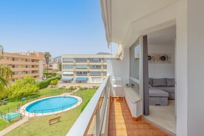 A balcony with a view of a swimming pool, a grassy area, and a building complex in the background.