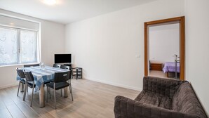 A dining area with a table and chairs, a television, and a mirror reflecting a bedroom. - Apartment "Levico Al Corso Apartments" with Mountain View (Levico Terme)