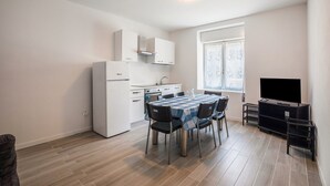 A compact kitchen with white appliances, a dining table with chairs, and a TV stand. - Apartment "Levico Al Corso Apartments" with Mountain View (Levico Terme)
