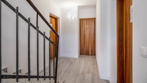 A hallway with a wooden door, a staircase with a metal railing, and a light switch on the wall. - Apartment "Levico Al Corso Apartments" with Mountain View (Levico Terme)
