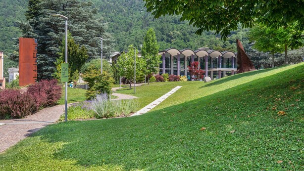A grassy area with a pathway leading to a building with a modern architectural design. - Apartment "Levico Al Corso Apartments" with Mountain View (Levico Terme)