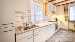 A kitchen with white cabinets, a double sink, a stove, and a window with a curtain. - Pet-Friendly Holiday Apartment 'Kuenz Dolomiten Drau' with Mountain View (San Candido)